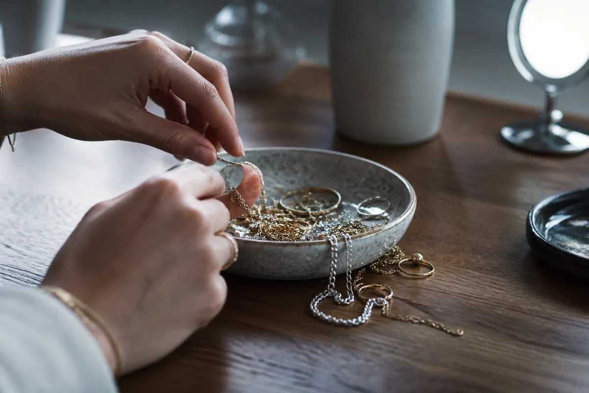 Bijoux dorés et argentés disposés dans une coupelle en céramique sur une coiffeuse