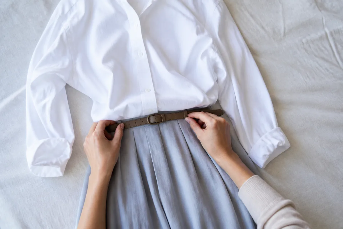 Tenue composée à plat : jupe midi, ceinture fine et chemisier posés sur un drap en lin